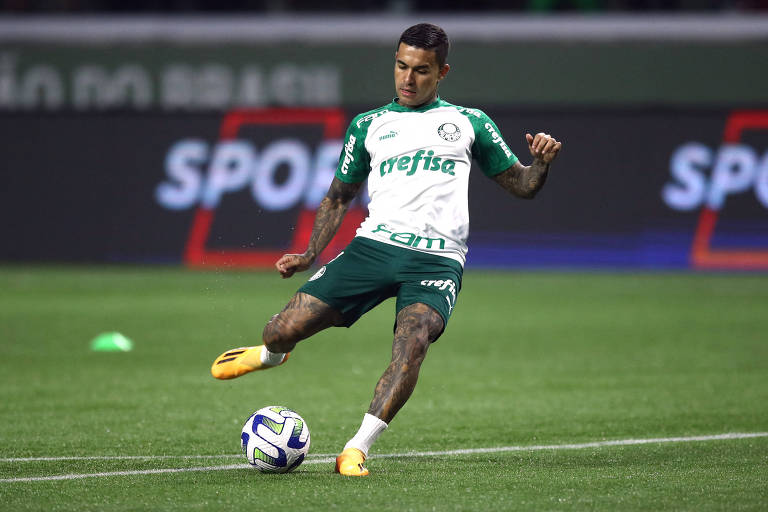 Atacante Dudu, do Palmeiras, vestido com o uniforme de aquecimento do clube, chuta bola de pé direito em campo de gramado sintético