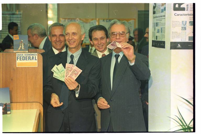 O então ministro da Fazenda, Rubens Ricupero, e o ex-presidente Itamar Franco mostram as cédulas de reais após troca das notas de cruzeiros reais em agência da Caixa Econômica Federal do Palácio do Planalto, em Brasília