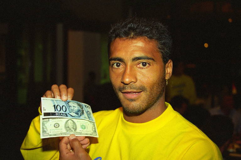 O hoje senador Romário segura duas cédulas, uma de R$ 100 e outra de US$ 100 para sinalizar a paridade