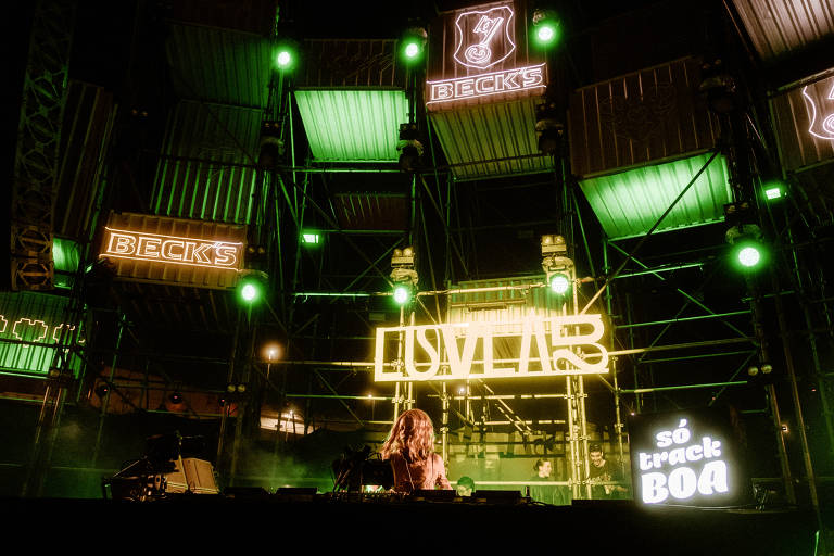 Palco com iluminação com os escritos "LuvLab" e DJ toca ao centro