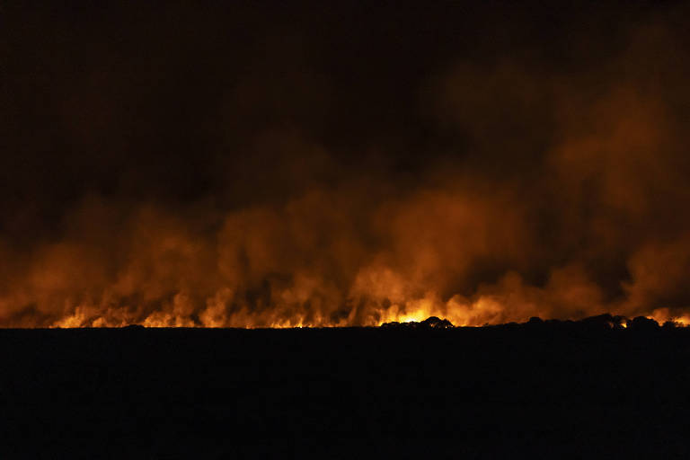 foto noturna mostra linha chamas que corta o meio da imagem, com fumaça subindo 