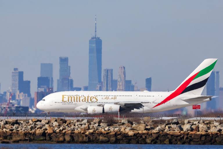 Avião visto de lado, marcado com as palavras "Emirates" e as cores da bandeira dos Emirados Árabes Unidos, verde, vermelho e preto, estampadas na cauda