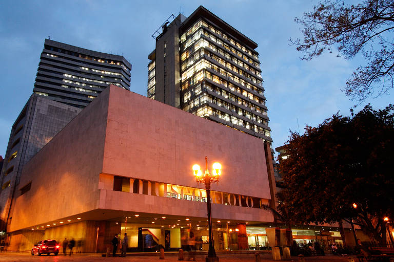 Fachada do Museu do Ouro, em Bogotá, está iluminada por uma luz laranja que vem do solo. Ao fundo, é possível ver prédios da região central, com as janelas acesas