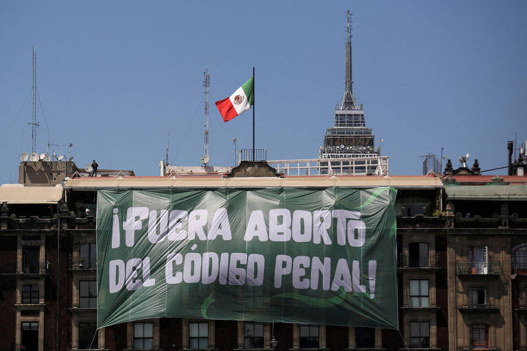 Uma grande faixa com a inscrição "¡FUERA ABORTO DEL CÓDIGO PENAL!" é exibida em um edifício, com a bandeira do México ao fundo, simbolizando um protesto pela remoção do aborto do código penal do país
