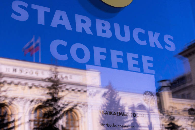A imagem mostra o reflexo de um edifício e uma bandeira russa em uma janela com a marca Starbucks Coffee.