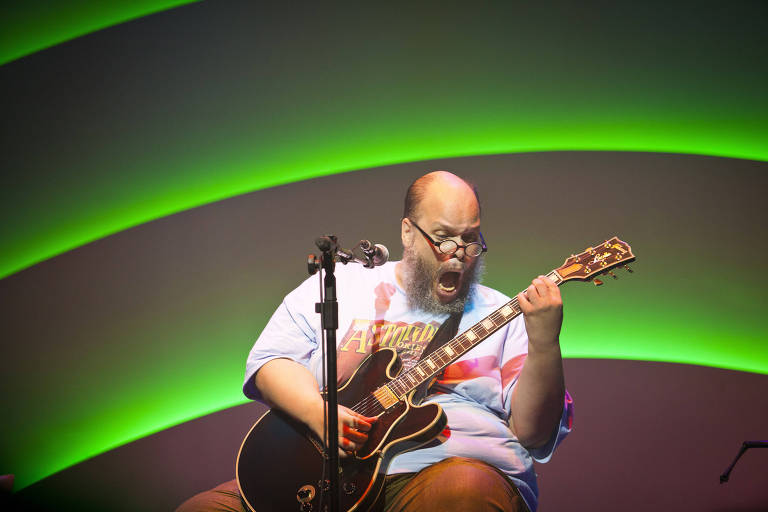 Em foto colorida, Ed Motta aparece cantando e tocando guitarra
