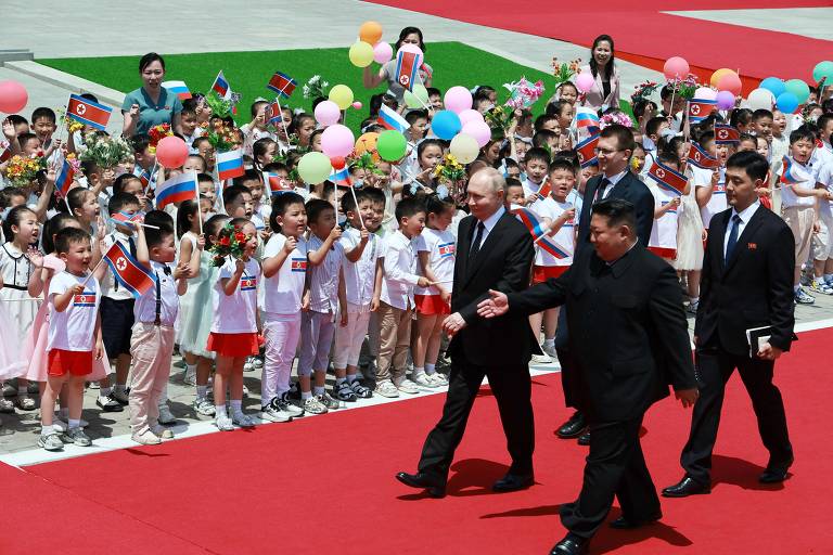O ditador norte-coreano, Kim Jong-un, e o presidente russo, Vladimir Putin, caminham enquanto são saudados pela população, a maioria crianças, em Pyongyang