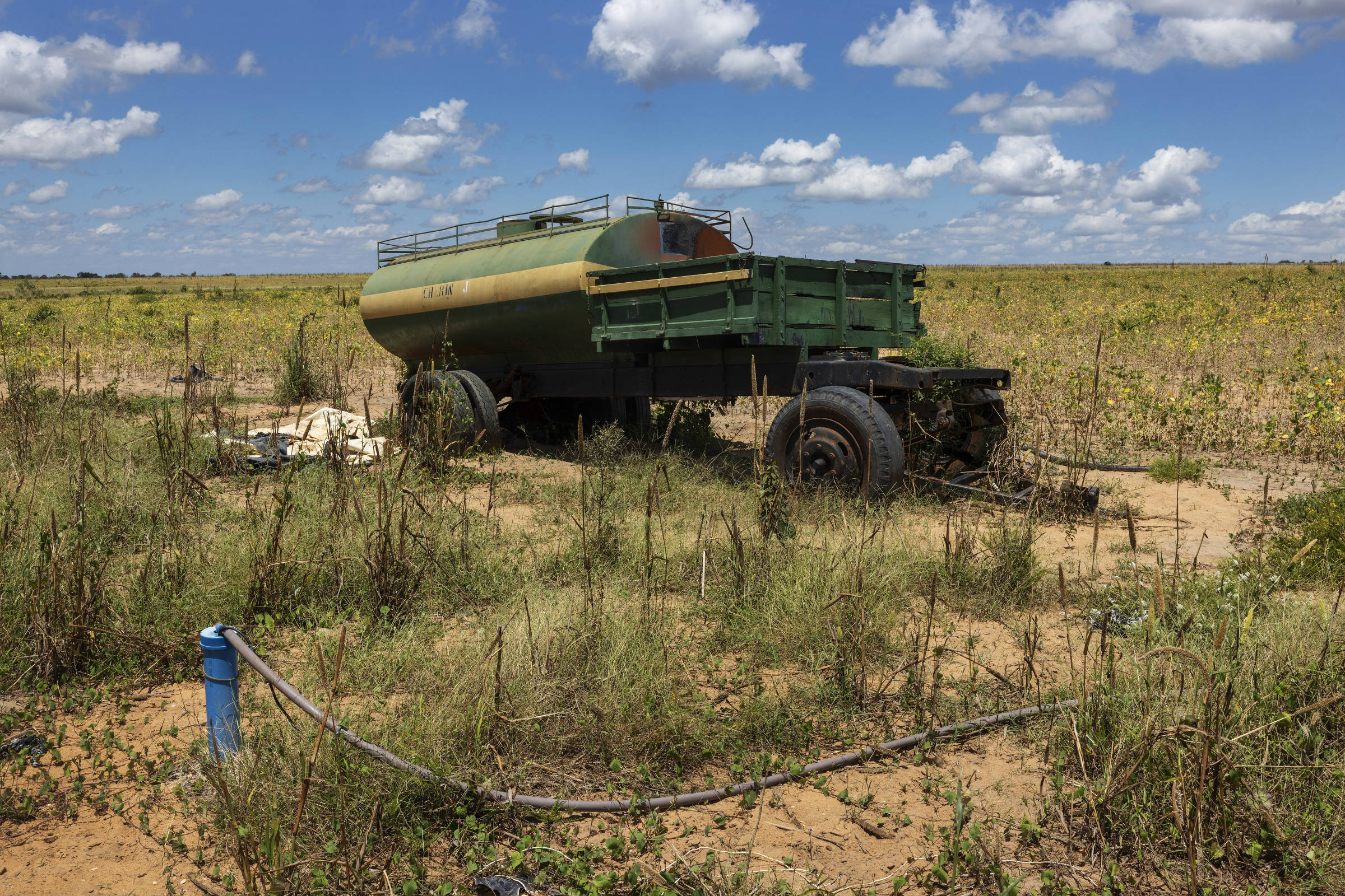 Carroceria de caminhão-tanque em meio a uma esparsa plantação de soja e ao lado da saída de um poço