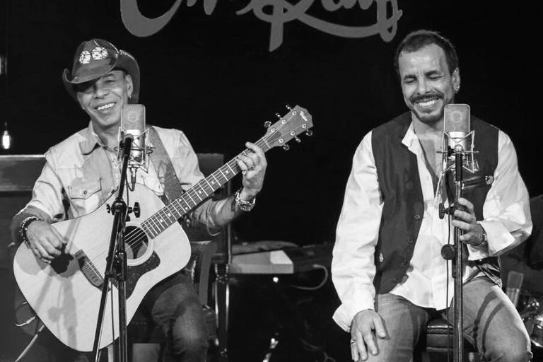 Dois homens, um deles de chapéu, se apresentam num show