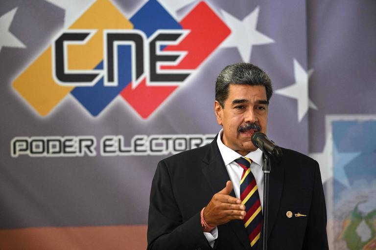 Maduro, de terno preto, camisa branca e gravata listrada, está falando em um microfone. Atrás dele, há um banner com o logotipo do CNE (Conselho Nacional Eleitoral) em cores azul, vermelho e amarelo, e o texto 'Poder Eleitoral'.