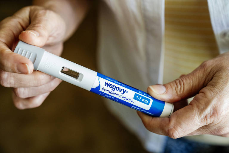 A imagem mostra uma pessoa segurando uma caneta de injeção com a marca 'Wegovy'. A caneta é branca com detalhes em azul e possui a inscrição 'semaglutide injection 1.7 mg