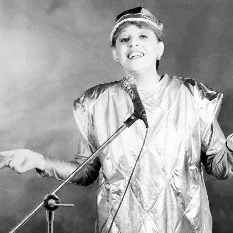 A imagem em preto e branco apresenta uma cantora com um microfone posando para a foto enquanto canta.