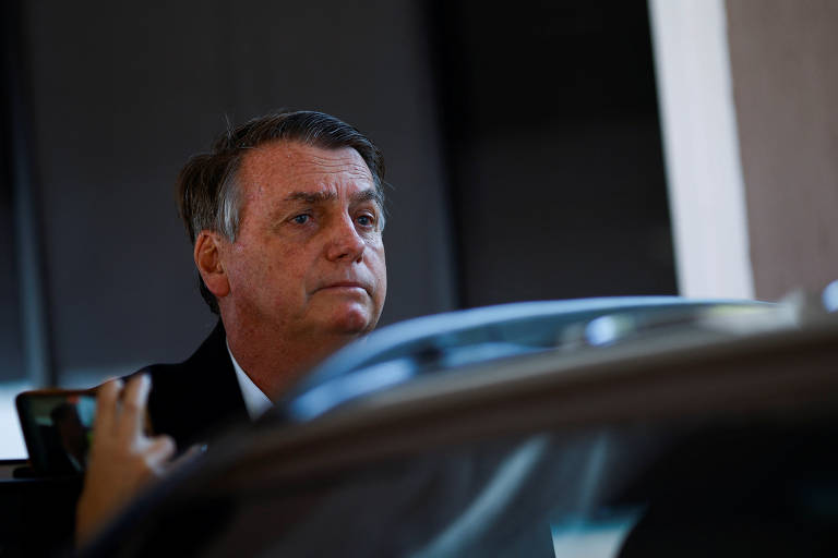 Foto mostra o rosto de Bolsonaro, um homem branco com cabelos grisalhos e rusgas tentando entrar em um carro