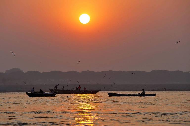 Três canoas navegam pelo rio Ganges ao entardecer