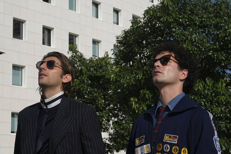 A imagem mostra dois homens usando óculos de sol e olhando para cima.