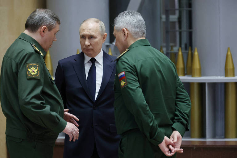Homem loiro e calvo, de terno escuro, cercado por dois militares em uniforme verde