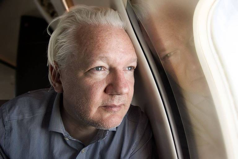 Um homem de cabelos grisalhos está sentado em um avião, olhando pela janela. Ele parece pensativo e está vestindo uma camisa de cor clara. A luz do sol entra pela janela, iluminando parcialmente seu rosto.