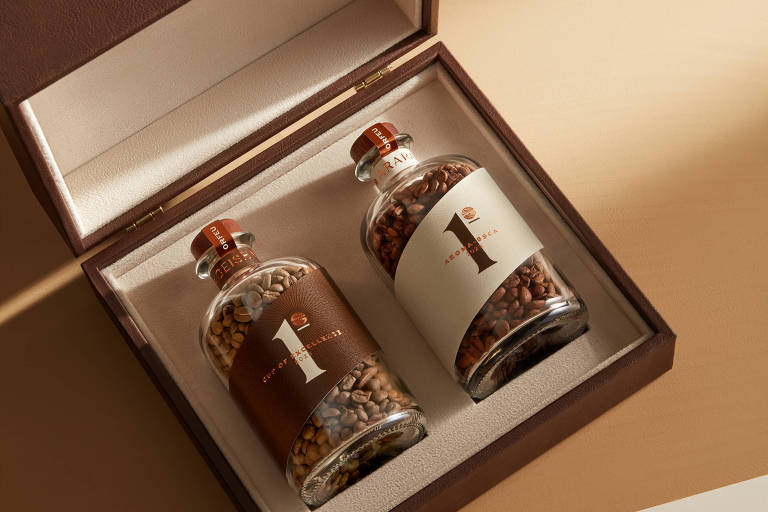 Duas garrafas de vidro com grãos de café dentro de uma caixa marrom com interior branco