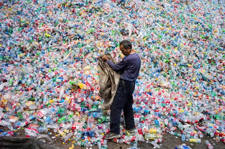 Trabalhador diante de montanha de garrafas plásticas numa usina de reciclagem nos arredores de Beijin, na China