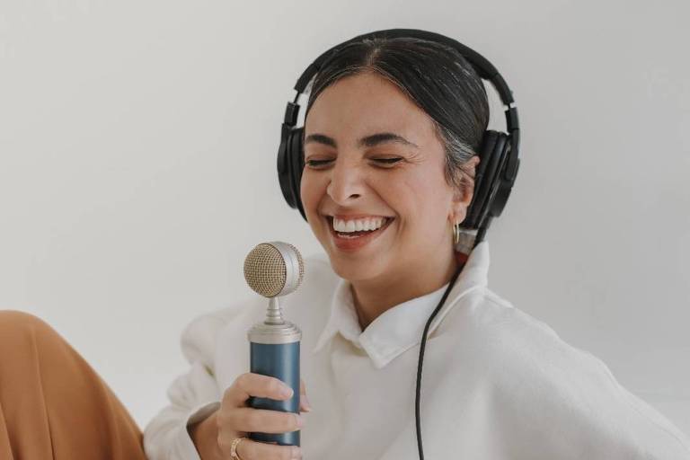 mulher sorrindo enquanto usa fones de ouvido grandes e segura um microfone. 