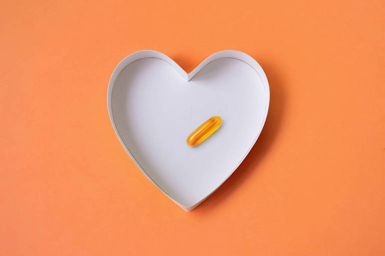 A imagem mostra uma cápsula amarela dentro de uma bandeja branca em forma de coração, sobre um fundo laranja.
