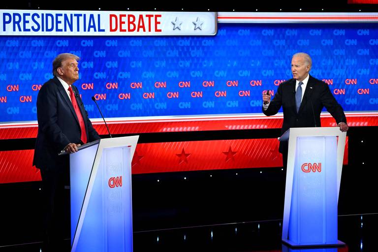 A imagem mostra dois homens em pé atrás de púlpitos com o logotipo da CNN, participando de um debate presidencial. O fundo é azul com o logotipo da CNN repetido várias vezes. No topo, há um banner que diz 'PRESIDENTIAL DEBATE' com duas estrelas ao lado.