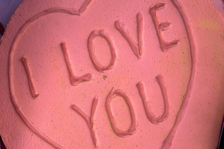 A imagem mostra uma superfície rosa com a mensagem 'I LOVE YOU' escrita em relevo dentro de um contorno de coração. As letras e o contorno do coração parecem ter sido feitos com uma substância espessa, possivelmente tinta ou massa.