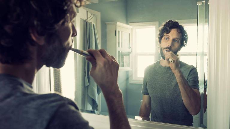 Homem escovando os dentes em frente a espelho