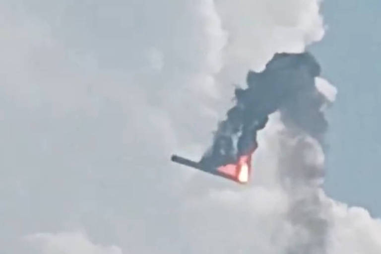 A imagem mostra um foguete em queda, com uma trilha de fumaça escura. Há chamas visíveis na parte inferior do foguete. O céu ao fundo está parcialmente nublado.
