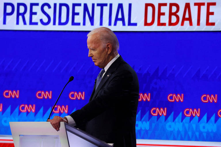 A imagem mostra Joe Biden de terno escuro e gravata, de pé atrás de um púlpito, durante um debate presidencial. No fundo, há um grande letreiro com as palavras 'PRESIDENTIAL DEBATE' em letras maiúsculas, com 'PRESIDENTIAL' em azul e 'DEBATE' em vermelho. O logotipo da CNN aparece repetidamente no fundo azul.