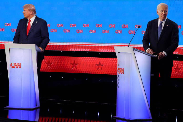A imagem mostra dois homens em pé atrás de púlpitos durante um debate presidencial transmitido pela CNN. O homem à esquerda está usando um terno escuro com uma gravata vermelha, enquanto o homem à direita está usando um terno escuro com uma gravata azul. O fundo é azul e vermelho com o logotipo da CNN repetido várias vezes.