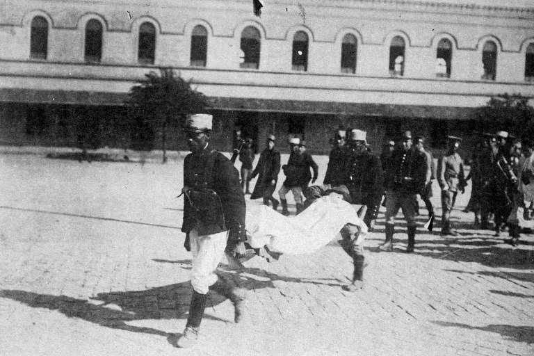 militares uniformizados transportam pessoa envolvida por lençol branco