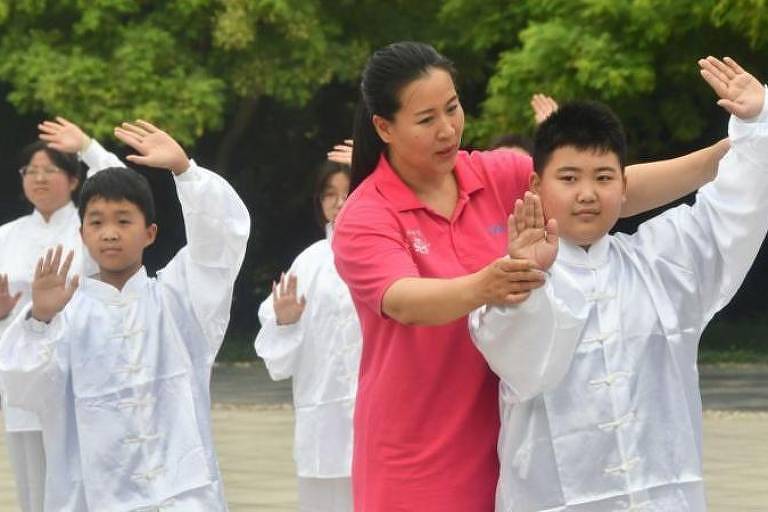 Professora ensina Tai Chi para crianças amarelas vestidas com roupinhas brancas
