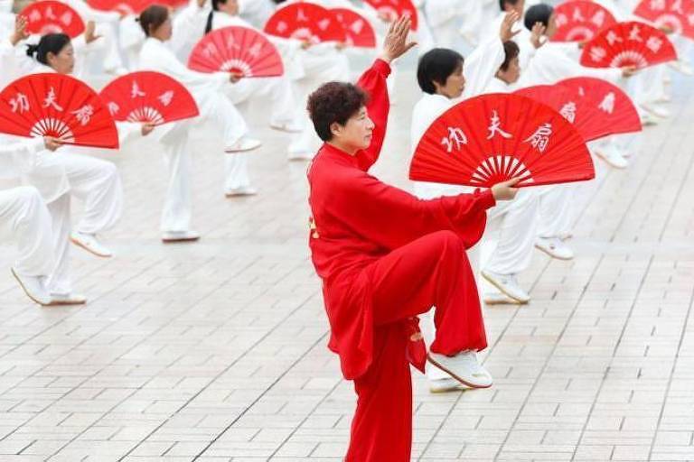Pessoas praticando tai chi em grupo vestidas de branco e vermelho
