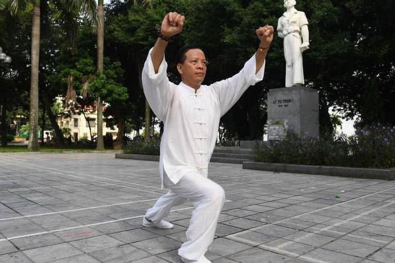 Fotografia mostra homem amarelo fazendo movimentos de arte marcial em uma praça
