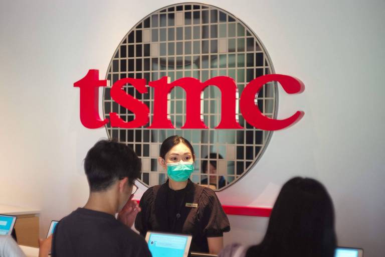 A imagem mostra a recepção da TSMC, com uma funcionária usando máscara facial verde e uniforme preto, atendendo duas pessoas. O logotipo da TSMC, em vermelho, está visível na parede ao fundo, com um design de wafer semicondutor atrás dele.
