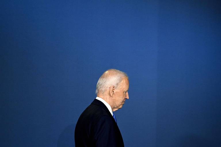 A imagem mostra Biden, um homem branco idoso de perfil, vestindo um terno escuro, contra um fundo azul. Ele tem cabelos brancos e está olhando para baixo.