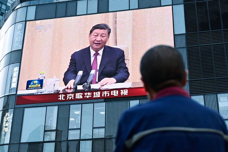 Um homem assiste a uma tela grande mostrando a cobertura de notícias do Presidente da China, Xi Jinping
