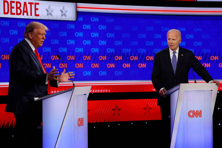 A imagem mostra Biden e Trump, dois homens em pé atrás de púlpitos durante um debate presidencial. O homem à esquerda, Trump, está gesticulando com as mãos, enquanto o homem à direita, Biden, está olhando para ele. O fundo é azul com o logotipo da CNN repetido várias vezes. Acima dos homens, há uma faixa branca com a palavra 'DEBATE' em vermelho e o logotipo da CNN.