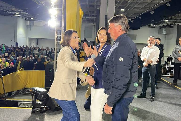 Os três estão em palco em frente a plateia de apoiadores, em um centro de convenções fechado