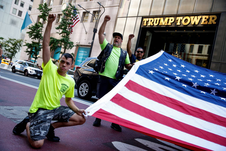 Um dia após o atentado contra Donald Trump, apoiadores dele seguram bandeira dos EUA em frente à Trump Tower, em Nova York