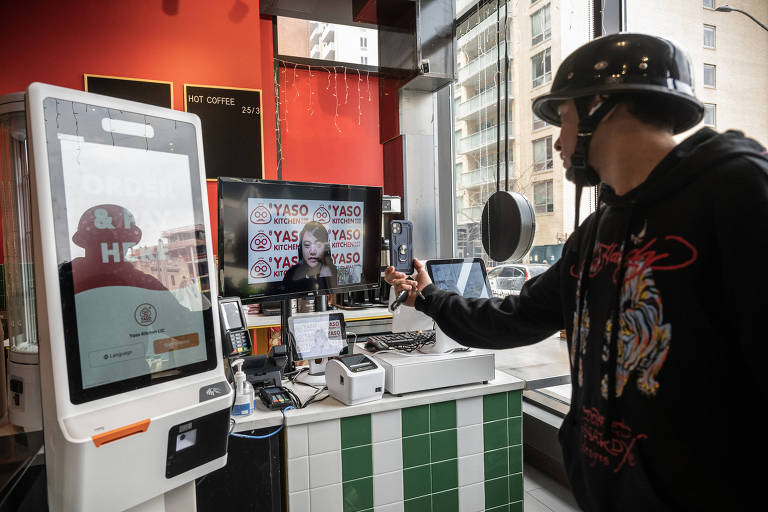 Um motorista de entrega interage com um caixa remoto enquanto aparece em uma tela em um outlet do Yaso Kitchen, um restaurante de bolinhos de sopa, em Nova York