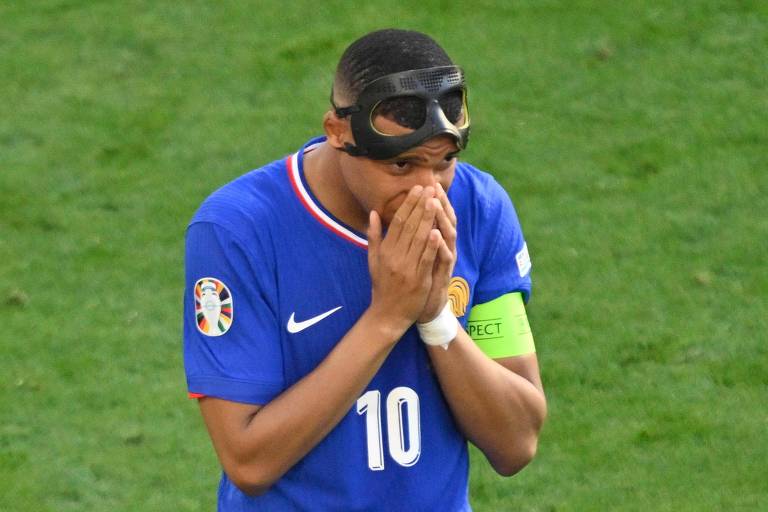 Mbappé, vestindo camisa azul da seleção francesa com o número 10 na parte da frente, a tarjeta de capitão no braço esquerdo e uma máscara de proteção na testa, põe as duas mãos em torno do nariz na partida contra a Polônia na Eurocopa da Alemanha
