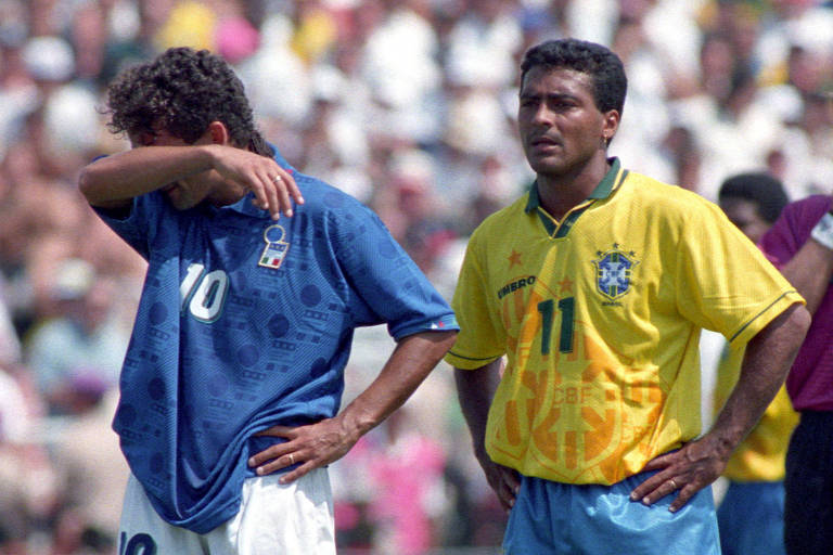 Na decisão da Copa do Mundo de 1994, nos EUA, Roberto Baggio, da Itália, vestindo camisa azul com o número 10, enxuga suor da testa com o braço direito; atrás dele, usando a camisa amarela com o número 11, está Romário, do Brasil, com as mãos na cintura