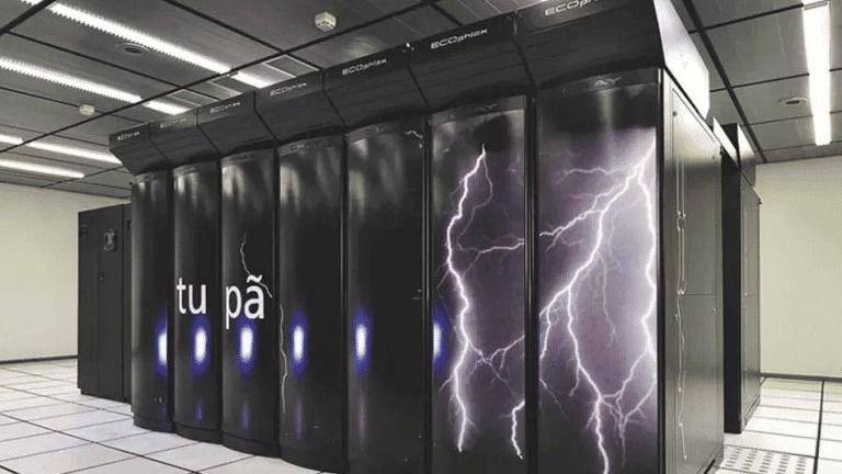 A imagem mostra um supercomputador chamado Tupã, localizado em uma sala de servidores. O gabinete do supercomputador é preto com imagens de raios brancos e a palavra 'tupã' escrita em branco