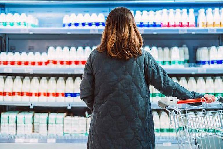 Mulher olhando para gôndolas com leite no mercado