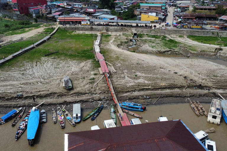 foto aérea mostra barcos em rio, com área seca ao fundo e casas