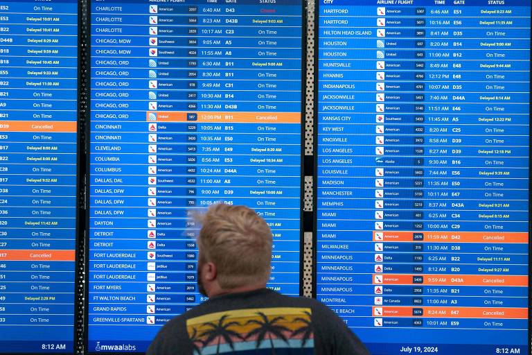 Homem loiro de camiseta estampada, à frente de painel com informações de voos