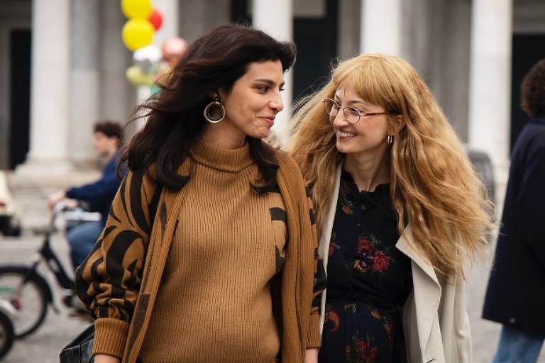 Em foto colorida, duas mulheres caminham pelas ruas de uma cidade