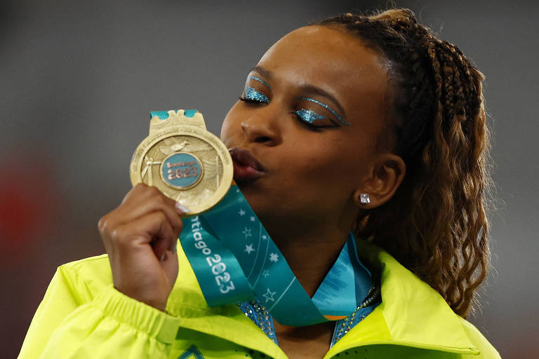 Com os olhos fechamos, a ginasta Rebeca Andrade segura com a mão direita a medalha de ouro conquistada na trave nos Jogos Pan-Americanos de 2023, em Santiago, no Chile, e dá um beijo nela
